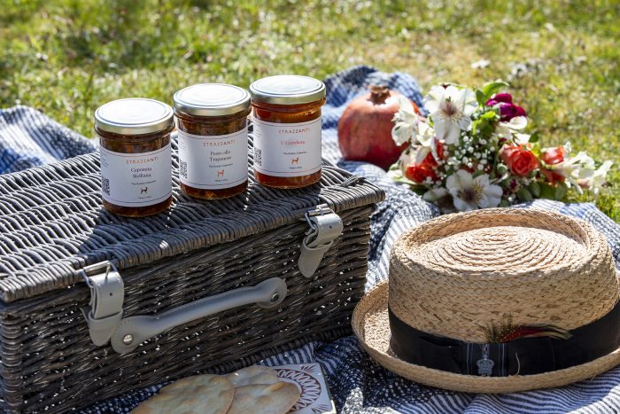Hamper of authentic Italian produce, three jars sitting on a picnic hamper outside on a picnic blanket.